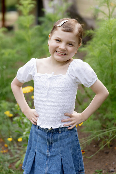 Little girl smiling with her hands on her hips as she stands outside