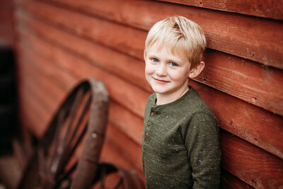 Five year old boy by a rustic building for his milestone portrait session.