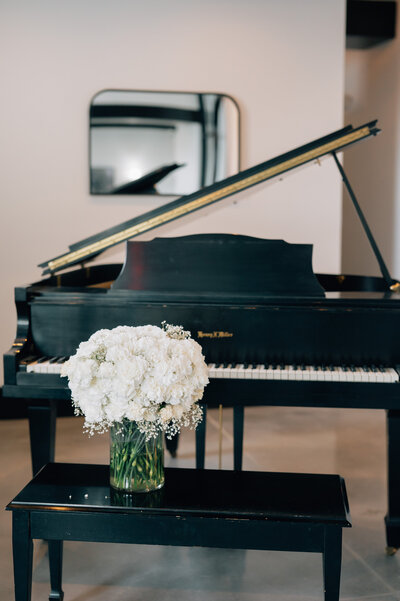 A bouquet of white roses sits on a piano bench at The Acreage. a wedding venue in Lincoln NE. Photo by Anna Brace who specializes in Lincoln NE Wedding Photography.
