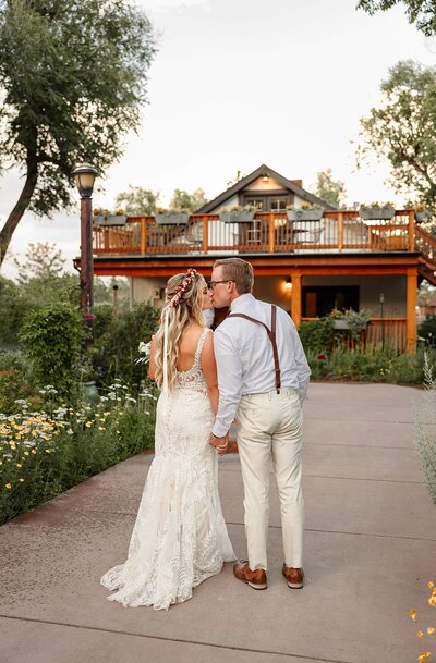 Bride and groom walking hand in hand kissing in a breathtaking Colorado Springs garden view, captured by Michelle Betz Photography, a Colorado Springs wedding photographer.