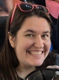 A close-up profile photo of the travel agent, smiling with red sun glasses perched on her head.