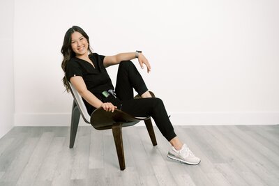 Woman smiling in a chair wearing black scrubs