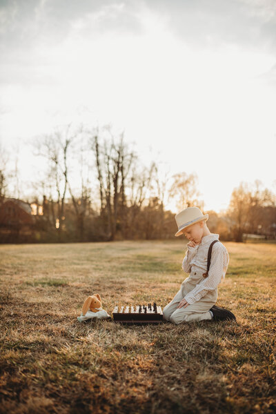 A little boy sitting in a field playing chess with his stuffed animal in Bluefield, West Virginia.