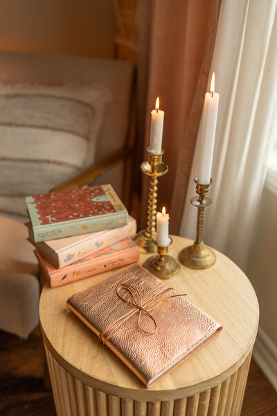 a side table with candles burning, a stack of pink and blue books and a small rose gold journal style photo album