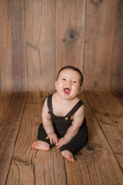 Milestone Photographer, a baby sits on wooden floors and smiles