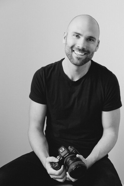 Photo of Andrew posing with his camera and smiling