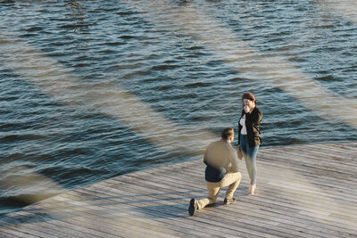A person kneeling down proposing to their partner on a dock