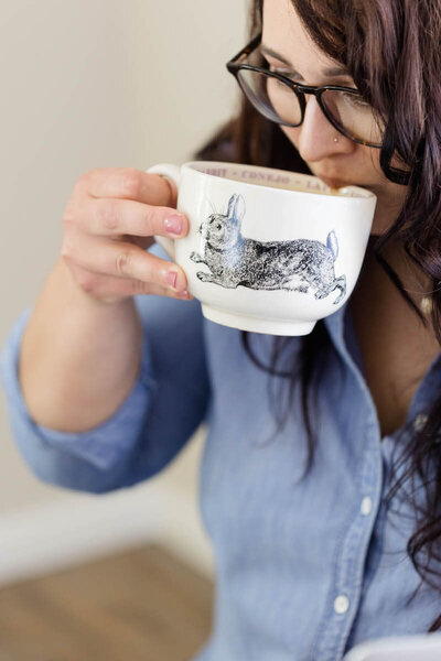 Aubre sipping coffee out of a wide mug with a rabbit illustration