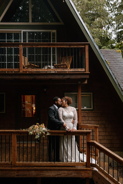 Bride and groom sharing a kiss on the porch of a cozy A-frame cabin in the Pacific Northwest during their intimate forest elopement.