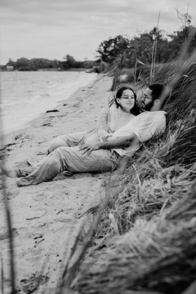 Black and white photo of pregnant wife and husband laying on the beach in Annapolis Maryland.