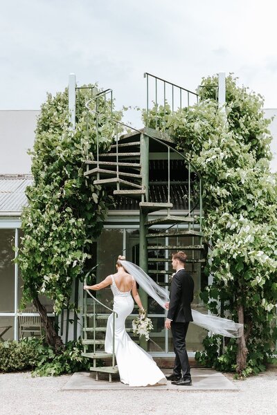 A bride and groom walking up a green spiral staircase.