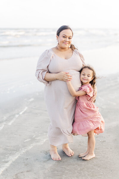 Mom and daughter both hug pregnant belly on the galveston beach