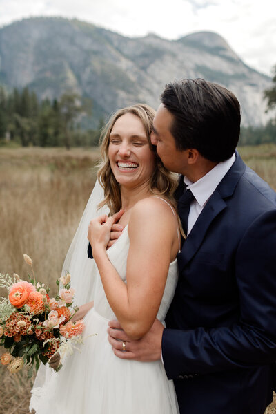 A groom holds his brides hand as he helps her walk down a rock in front of a beautiful lake view on their mammoth lakes wedding day. 