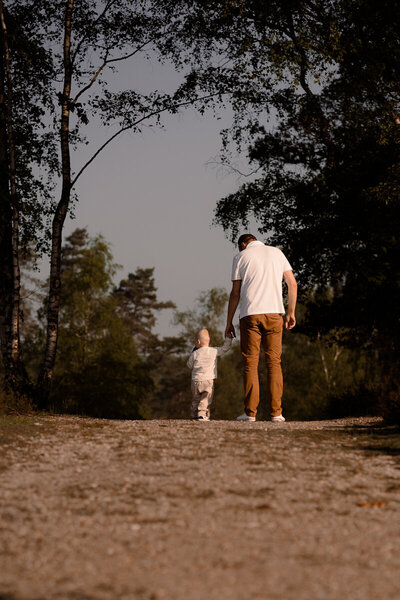 Vader en zoon lopen hand in hand in de zon tijdens een gezinsshoot