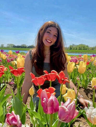 Brunette stands in field of colorful tulips and smiles at camera on a sunny day