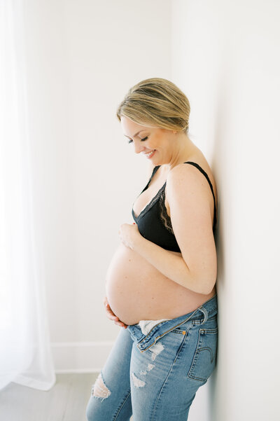 Expecting mama holds belly and laughs in Raleigh photography studio during maternity session