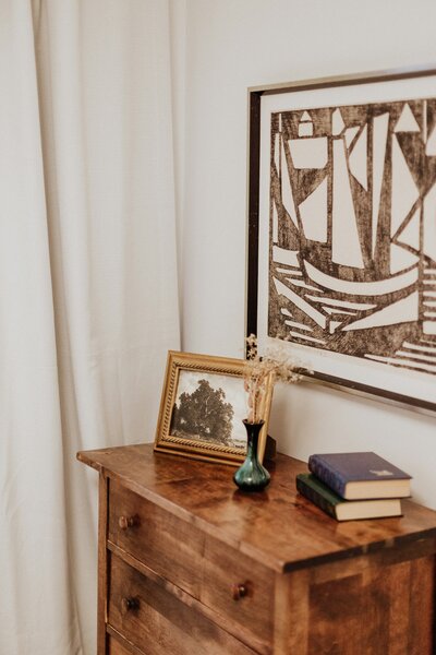 An antique dresser with decorative accessories and wall art hanging above the furniture piece.