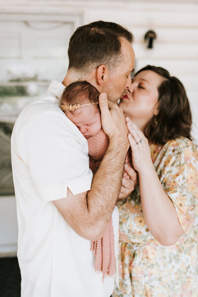 Embrace the heartfelt beauty of family love in North Texas as a newborn daughter becomes the center of adoration for her utterly smitten parents. This touching image encapsulates the profound love shared by the mother and father as they lovingly cradle their precious newborn. Against the backdrop of North Texas, witness the tender affection and overflowing joy of a family united by their newest arrival. Professional newborn photography portraying the unbridled love and warmth shared by a family in North Texas