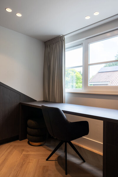 Strakke, functionele werkruimte met een warme houten vloer en een zwart maatwerkbureau dat perfect past in de nis onder het raam. Ideaal voor wie rust en focus wil combineren met een stijlvol interieur.