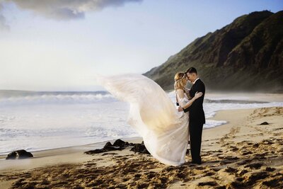 A bride and groom holding each other and looking at each other in Hawaii. The bride's dress is being blown in the wind