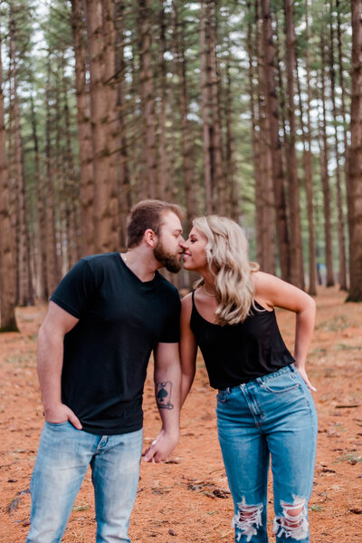 A couple poses holding hands and leaning into each other while standing in the middle of the Siloam Tall Pines.