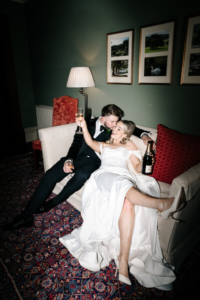 Bride and groom sharing champagne while laying on a couch