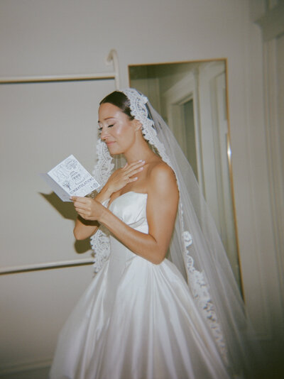 A bride in a lace mantilla veil holds back tears while reading a card before her Detroit wedding ceremony