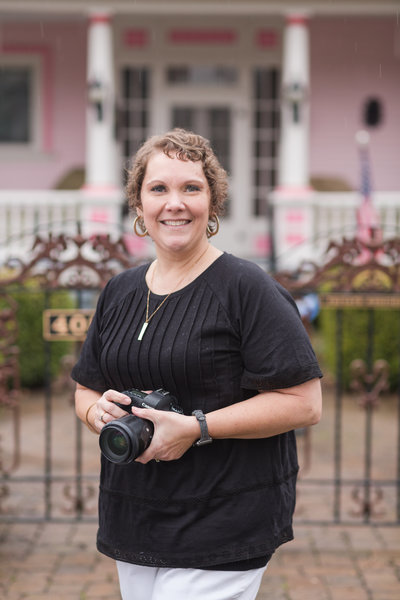 photographer standing in front of pink house holding camera for headshot
