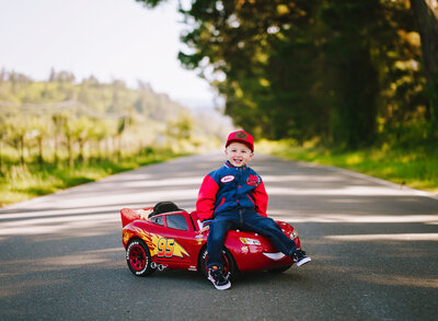 A one year old sitting on top of a play race car.