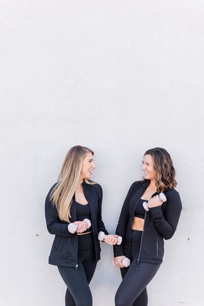 Two women in black fitness attire holding weights