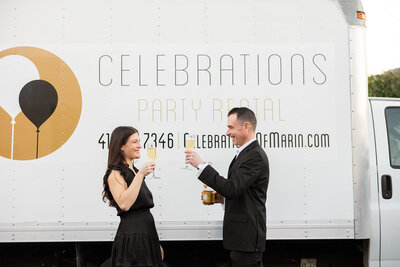 Two business owners standing in front of their event truck toasting with champagne glasses.