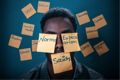 Picture of a man with post it notes on his face that say "Norms", "Expectation", and "Society"