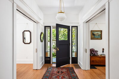 A black front door is open in a large entryway with a turkish rug and hanging light fixture, representing a home you can buy in Portland.