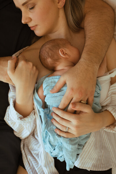 A newborn baby boy sleeping in his mothers arms , the father has wrapped his arms around both of them , in home session , Kingscliff and Tweed Heads