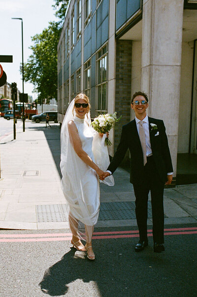 bride and groom walking and smiling, with sunglasses on, captured on 35mm film with grain