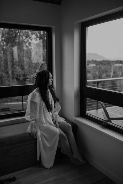 Bride sits looking out window in Alaska