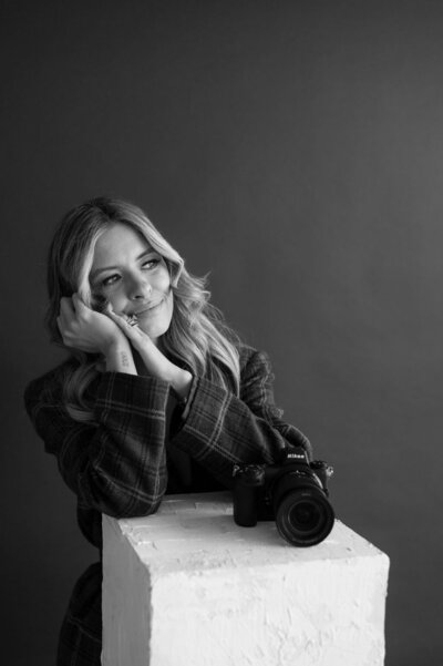 A black and white portrait of Emily resting her head on her hands as she looks off to the side.