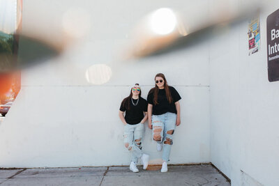 Two girls standing against a wall in jeans and black shirts