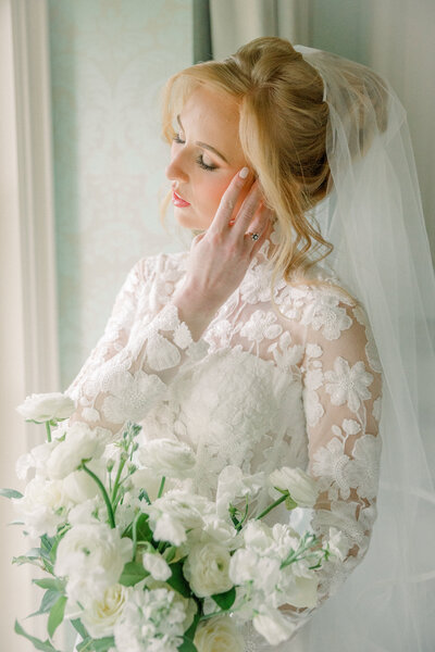 bride gently moving her hair while holding her neutral and greenery filled bouquet during bridal portraits