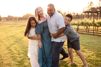 Candid outdoor family photo by a Portland, Oregon family photographer, showing parents and kids walking along a rocky riverbank at sunset.