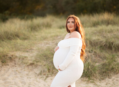 Maternity portrait of mum cradling bump among the sand dunes during golden hour in Studland, Dorset