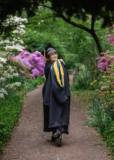 Posed photo of a woman wearing a graduation cap and gown in a New Jersey park in the spring.