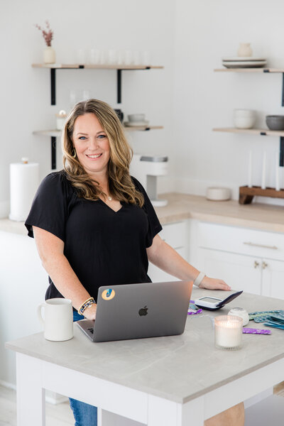 Woman in a kitchen working on a laptop during branding photoshoot.