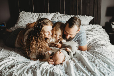 During an in-home newborn session, in North Mandan, ND a family snuggles together on the bed. 
