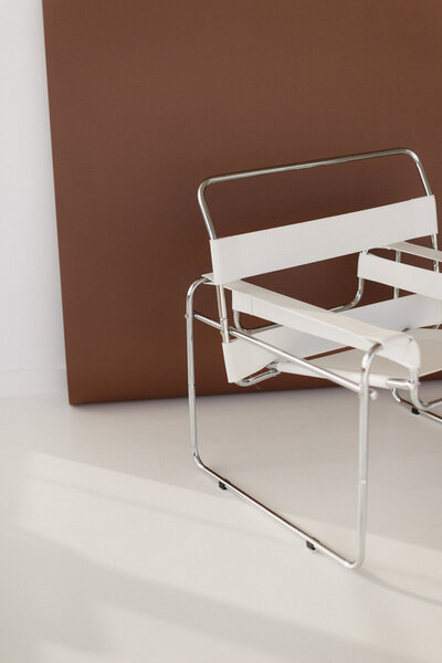 Minimalist product shot of a silver and white modern chair set against a warm brown backdrop in an all-white studio.