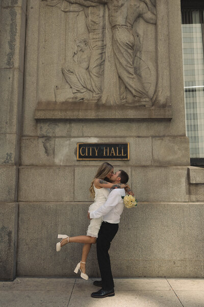 oyful moment of a newlywed couple sharing a kiss outside City Hall, celebrating their love and commitment in an intimate urban setting