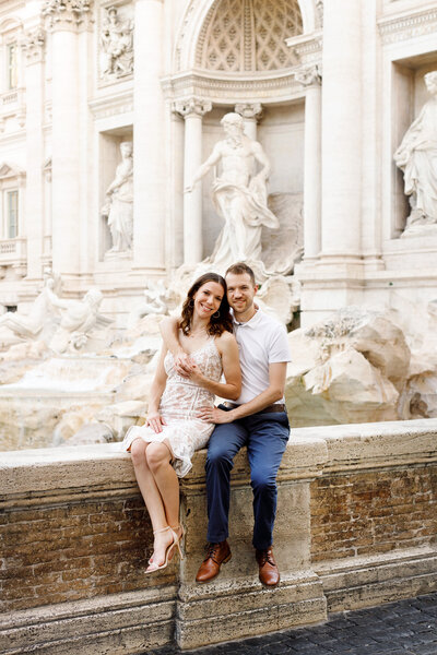 Couple sitting and embracing on the ledge of the Trevi Fountain. Taken by Rome Photographer, Tricia Anne Photography.