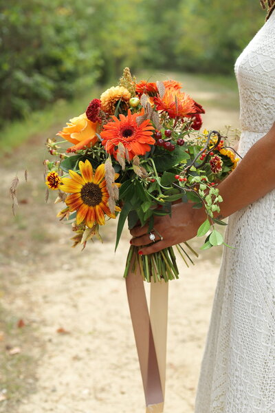 Bride holding a bouquet of fall colored florals on her wedding day in a white  lace dress