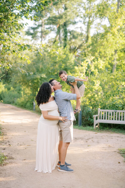 mother and father hold their young daughter in the air and smile
