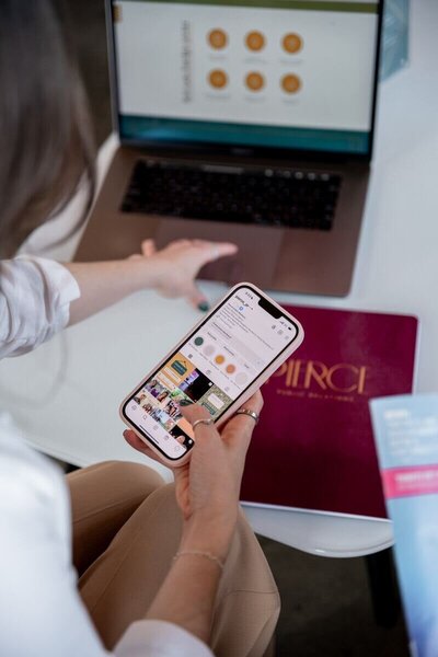 A team member browses Instagram on a phone while referencing a Pierce PR notebook and presentation on a laptop.